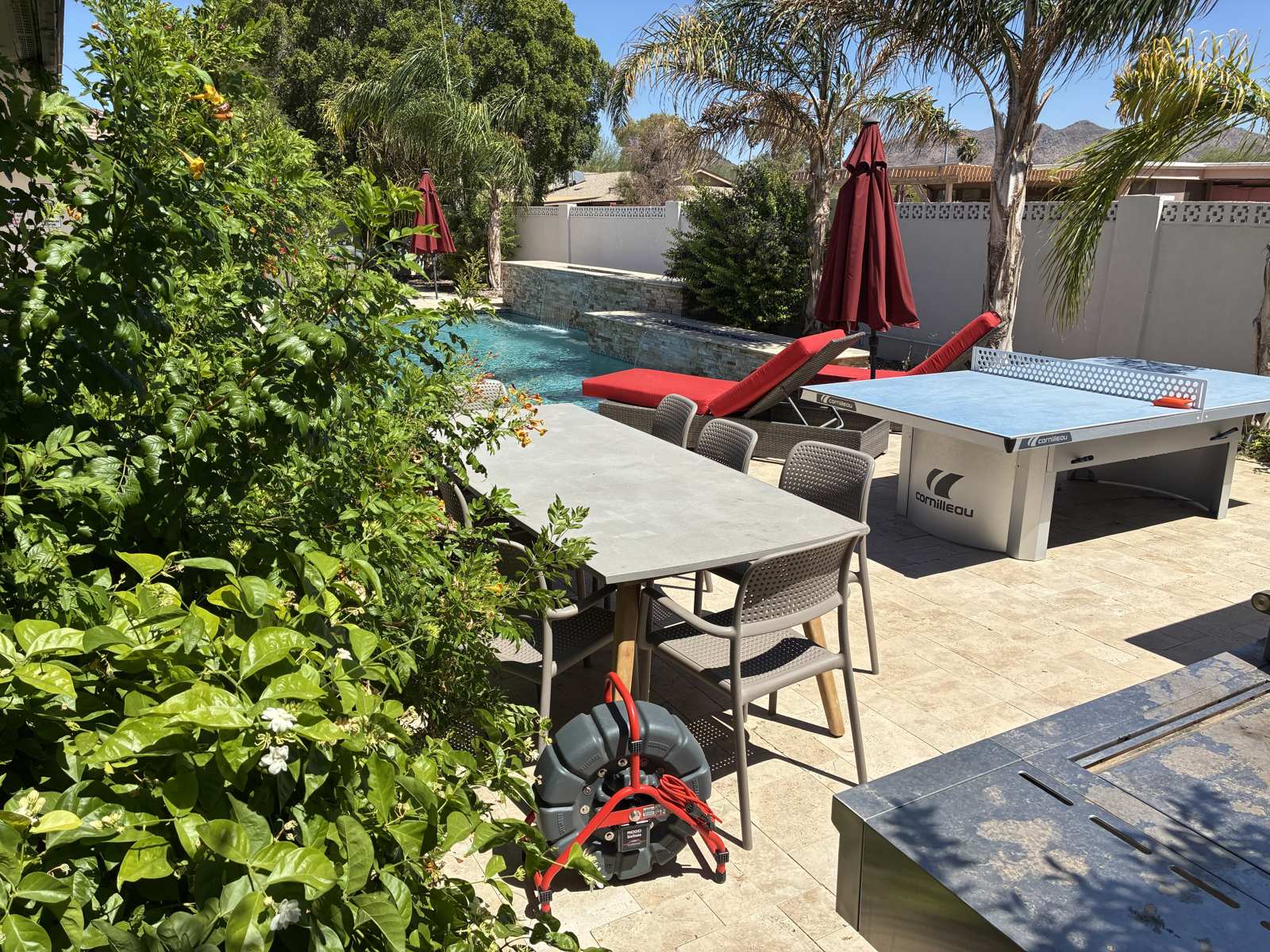 A sewer camera reel set up on a travertine pool deck beside a backyard pool
