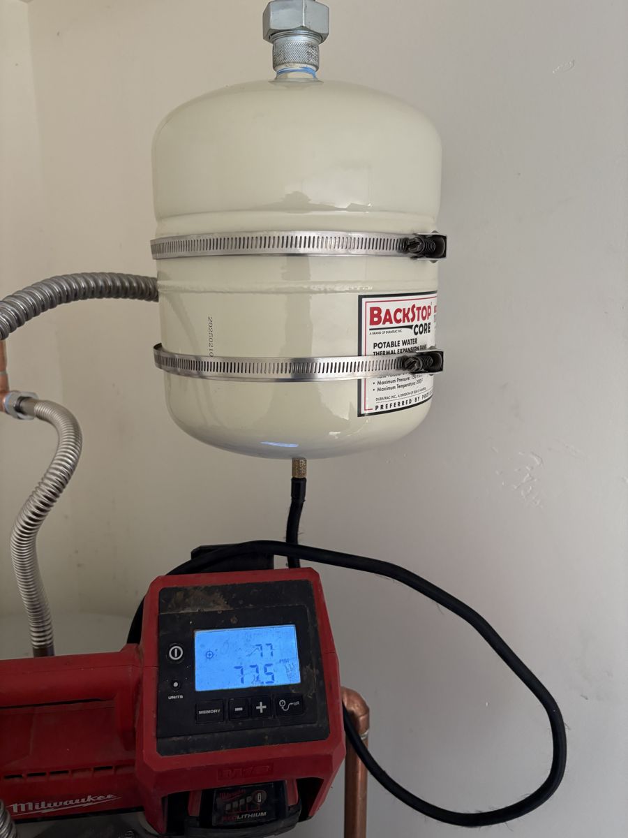 A thermal expansion tank installed above a water heater with a digital pressure gauge on the line