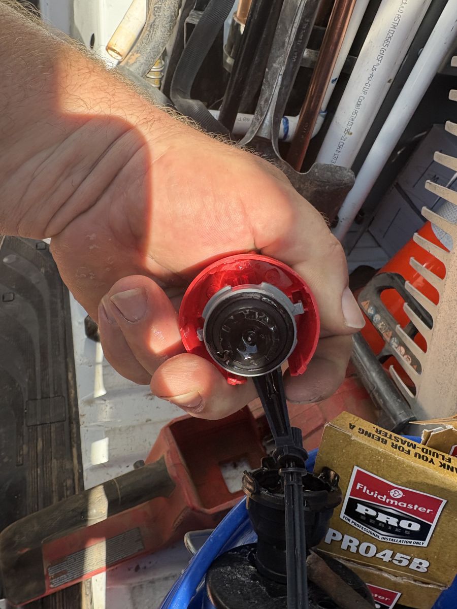 A plumber’s hand holding a new red toilet flapper inside the service van