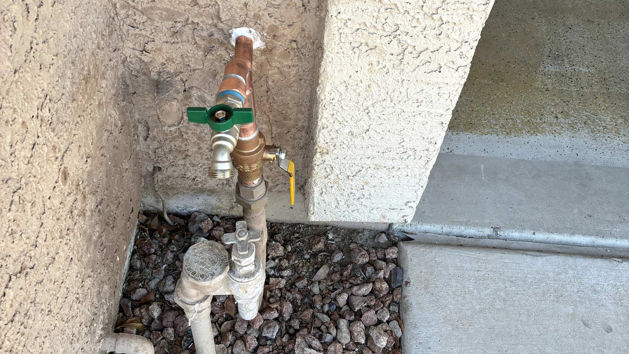 New copper hose bib and backflow assembly at the base of a stucco exterior wall
