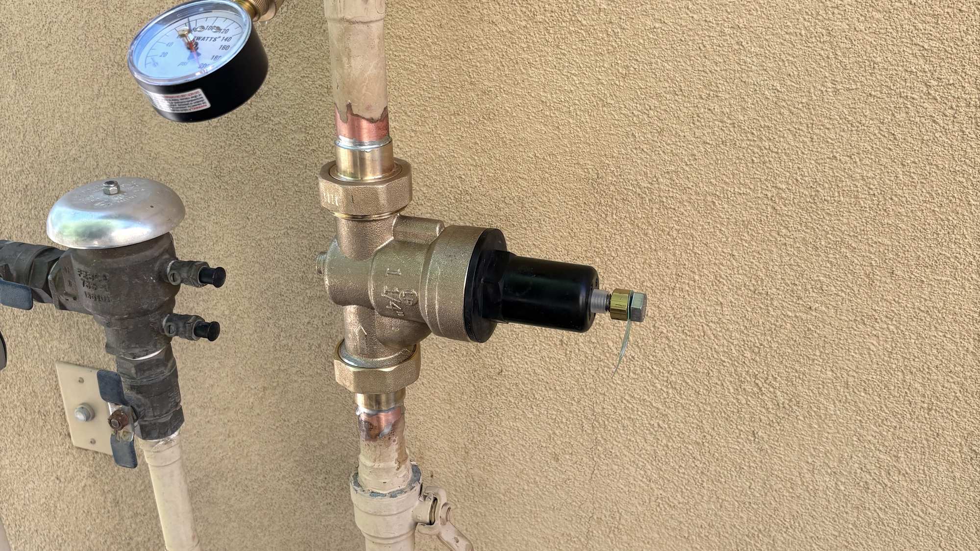 A newly installed brass pressure-reducing valve and test gauge on an exterior wall