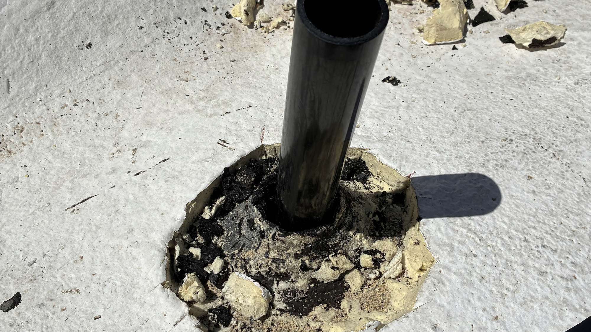 A sewer vent pipe reset through a flat roof with fresh sealant around the boot
