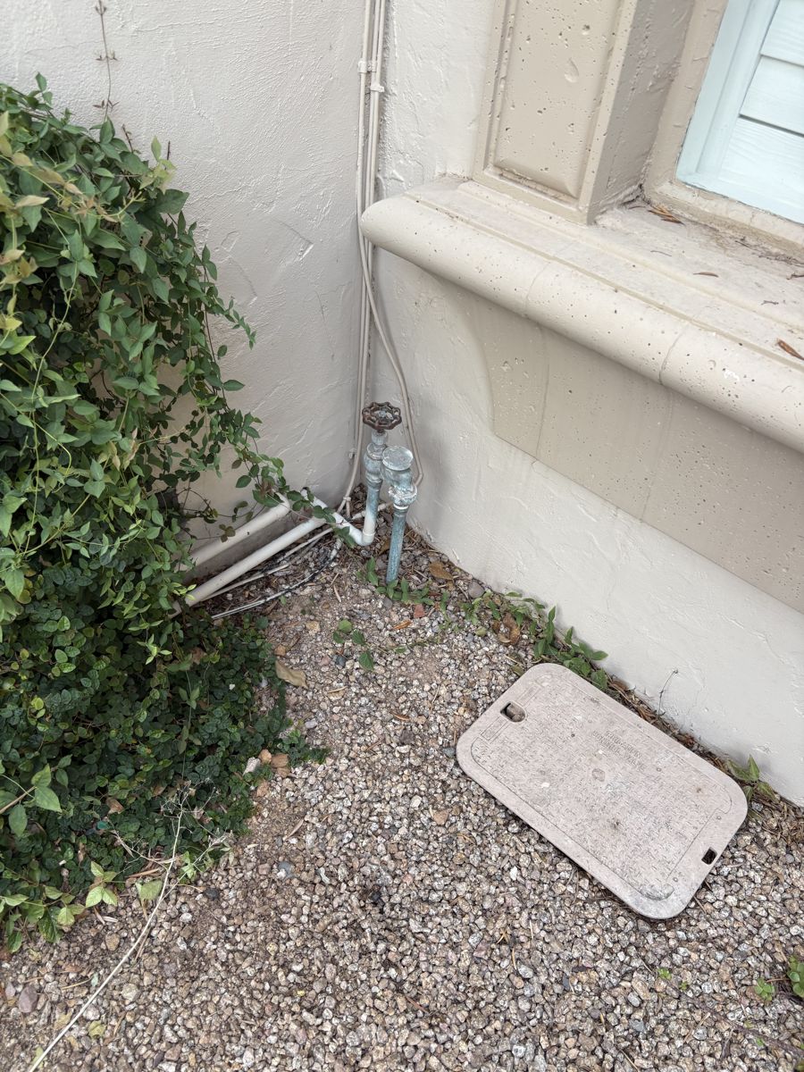 Exterior hose bib and backflow assembly beside an irrigation valve box at the base of a stucco wall