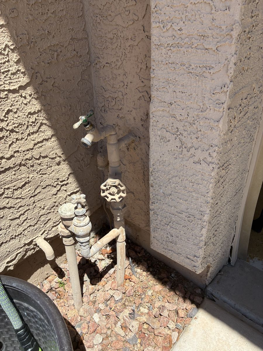 A dusty old exterior hose bib and pressure regulator on a stucco wall before replacement