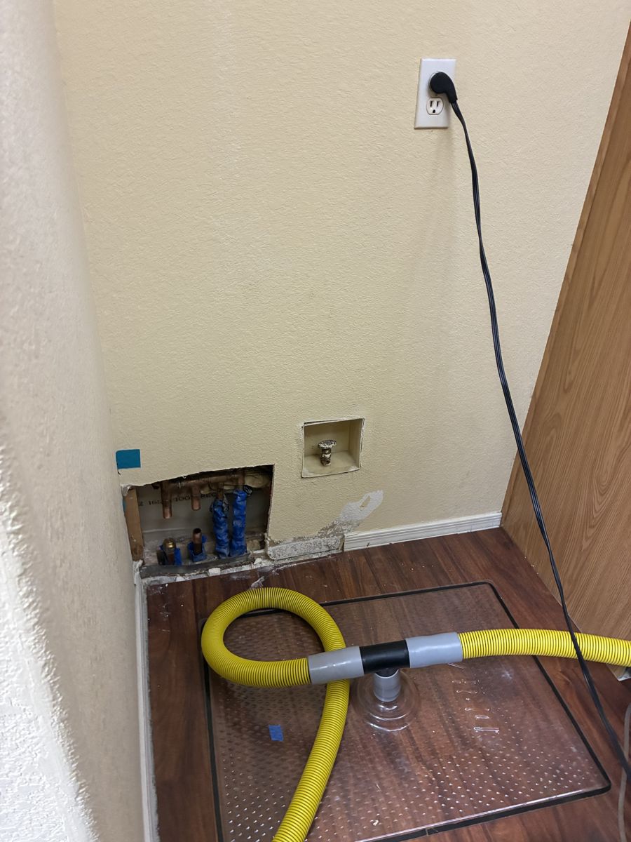 Laundry closet wall opened to the studs with copper stub-outs and a drying hose after a leak