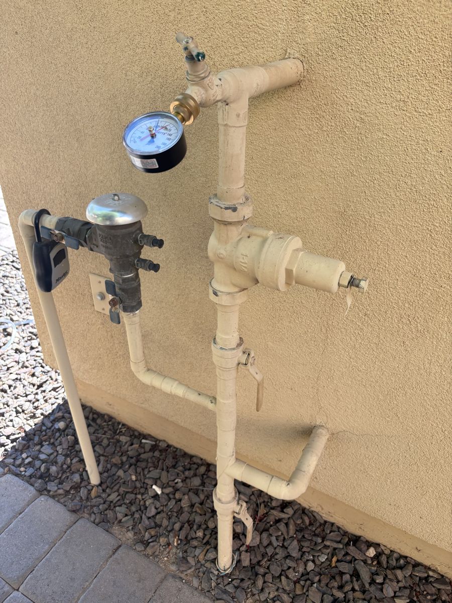 Exterior pressure regulator and backflow assembly on a stucco wall with a test gauge fitted to the hose bib