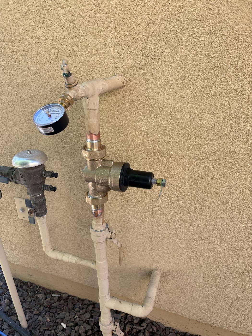 A newly installed brass pressure-reducing valve on an exterior wall, with a test gauge fitted above it