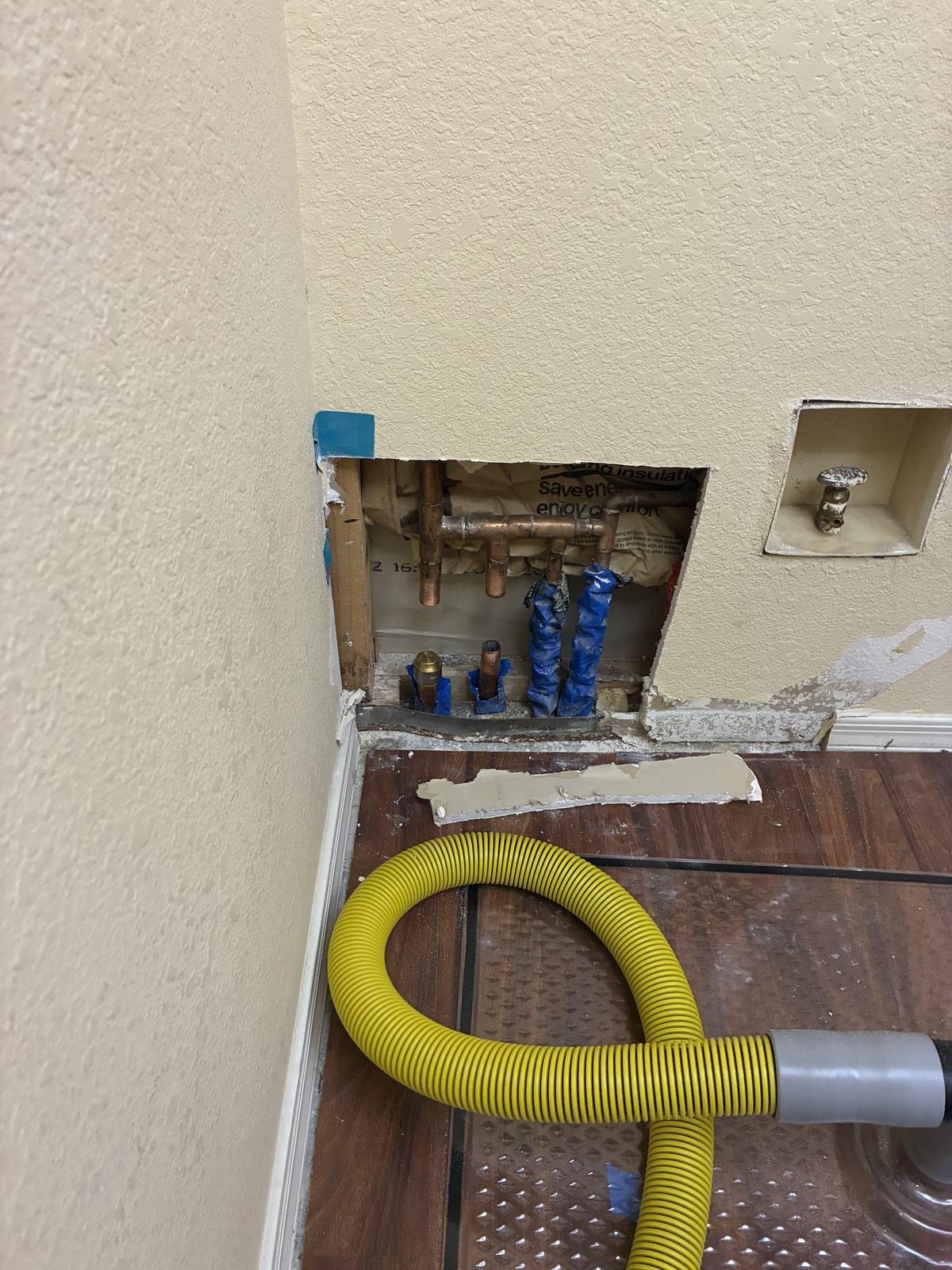 Opened interior wall with copper supply lines and a drying hose running to the cavity