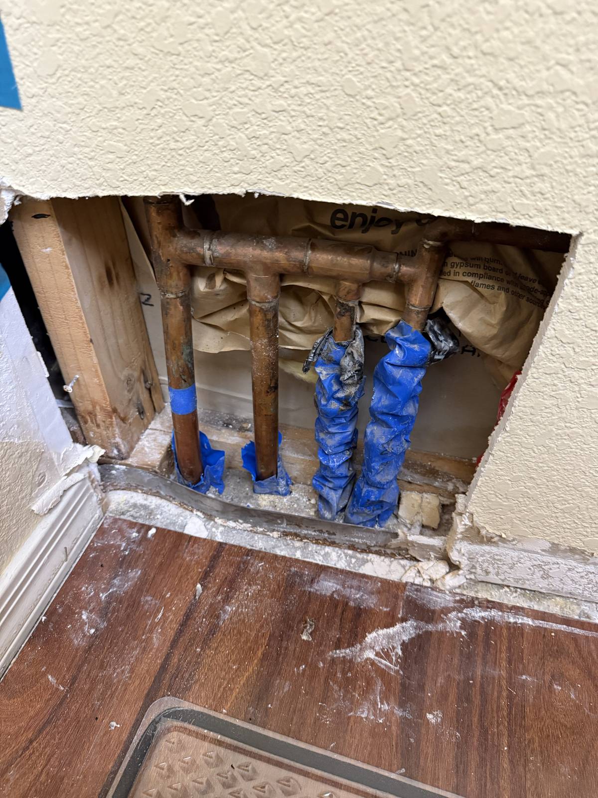 Copper supply manifold with blue-wrapped lines exposed in an opened interior wall during a repipe
