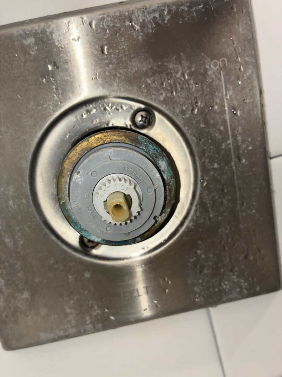 A shower valve with the handle removed, exposing a scaled cartridge before replacement