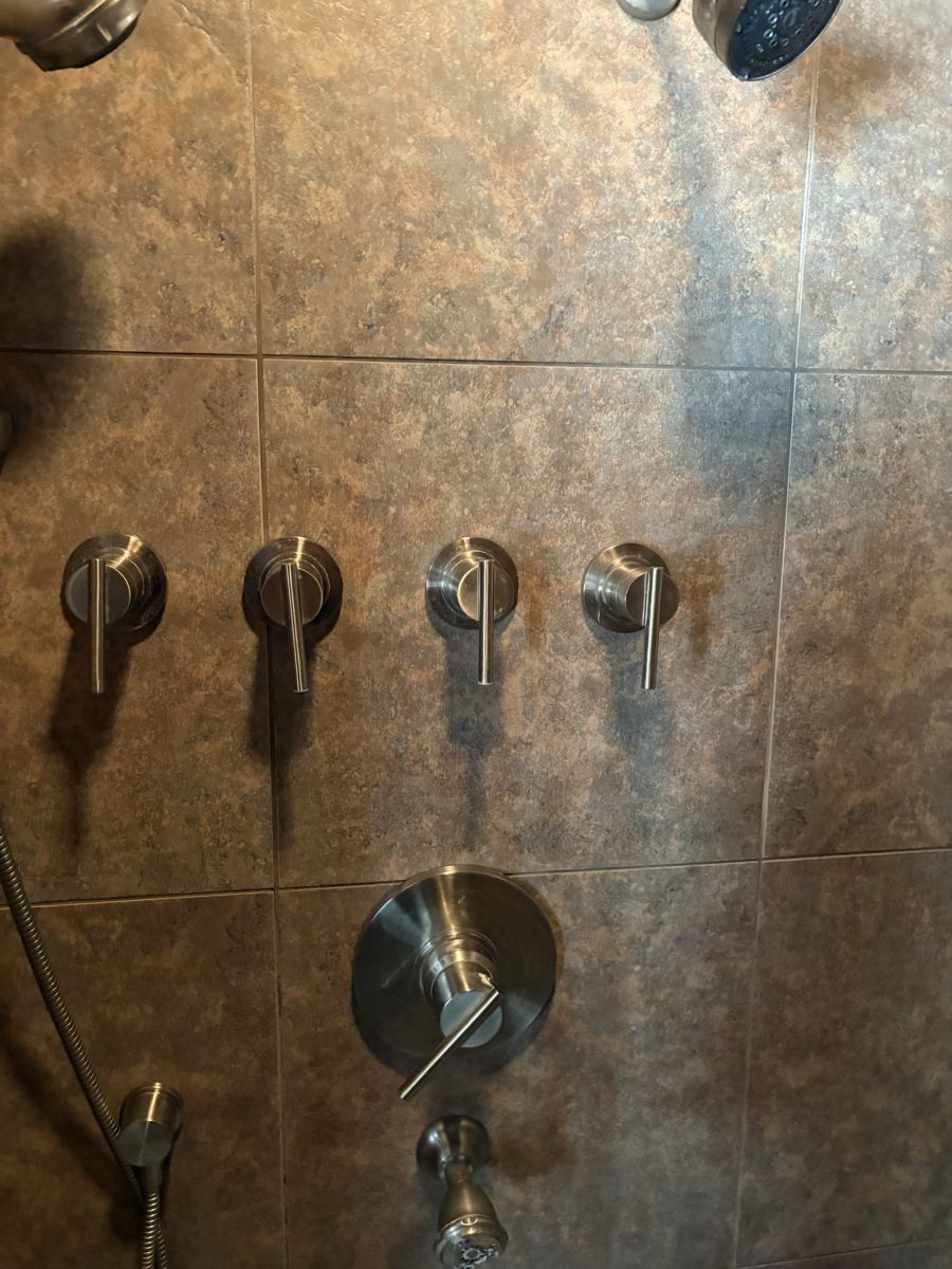 Four new shower volume controls and a diverter trim on a tiled shower wall