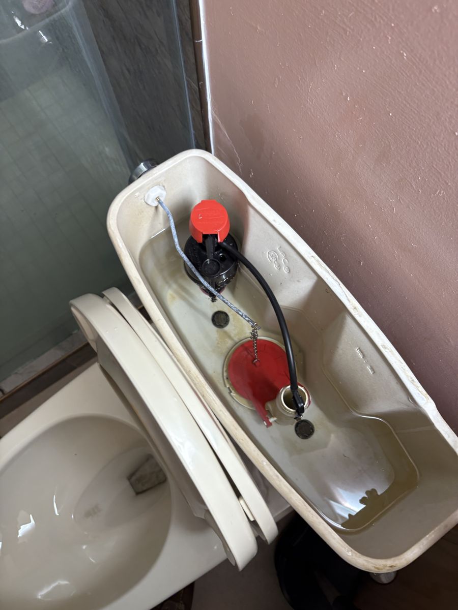 Inside a toilet tank after repair with a new red flapper and fill valve installed