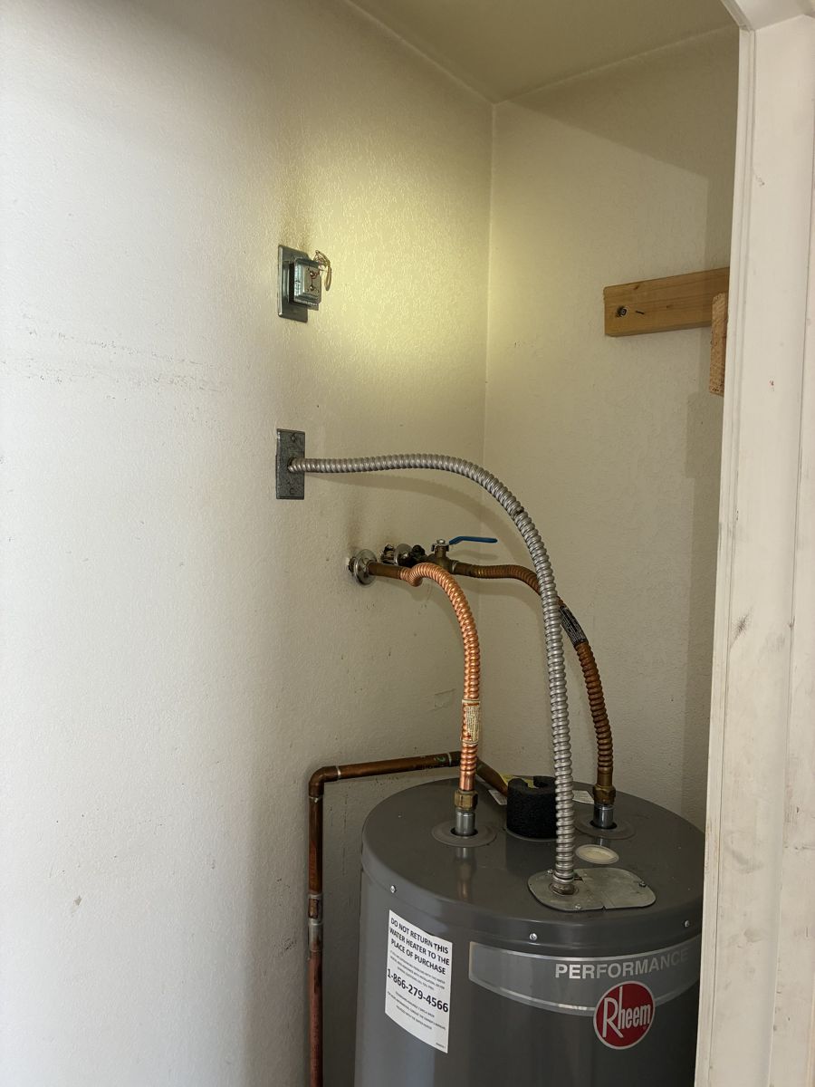 A newly installed electric water heater in an interior closet with flexible connectors and a drain pan