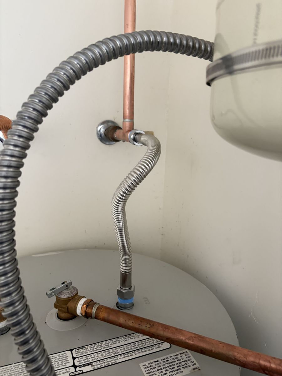 The top of a water heater with flexible water connectors, a temperature and pressure relief valve and the expansion tank above
